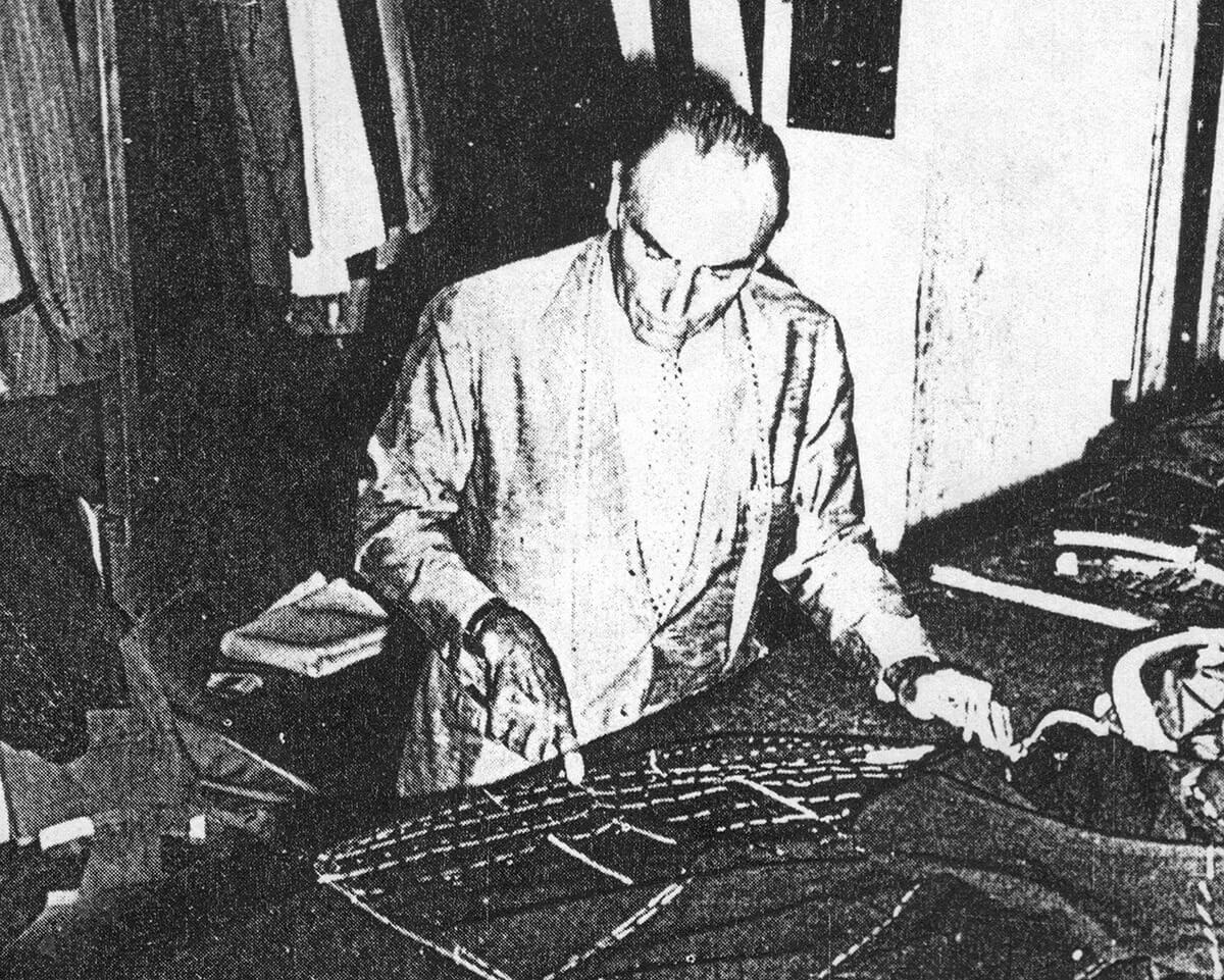 Archival black-and-white photograph of Vincenzo Attolini cutting cloth at a table.