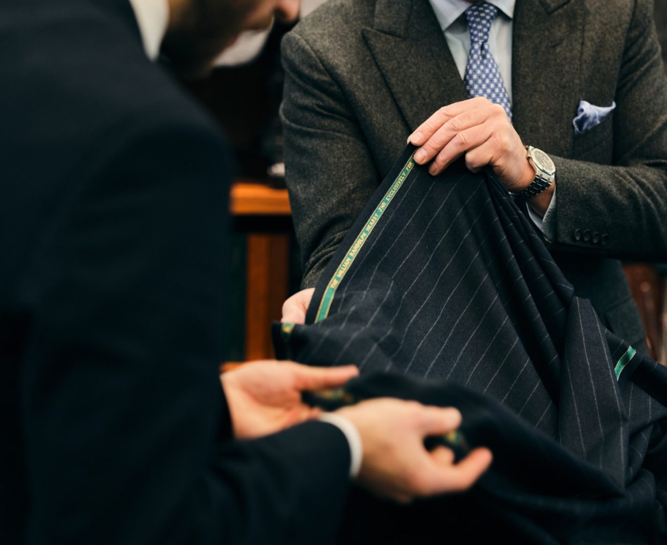 Two men considering a dark pinstriped cloth at Henry Poole & Co.