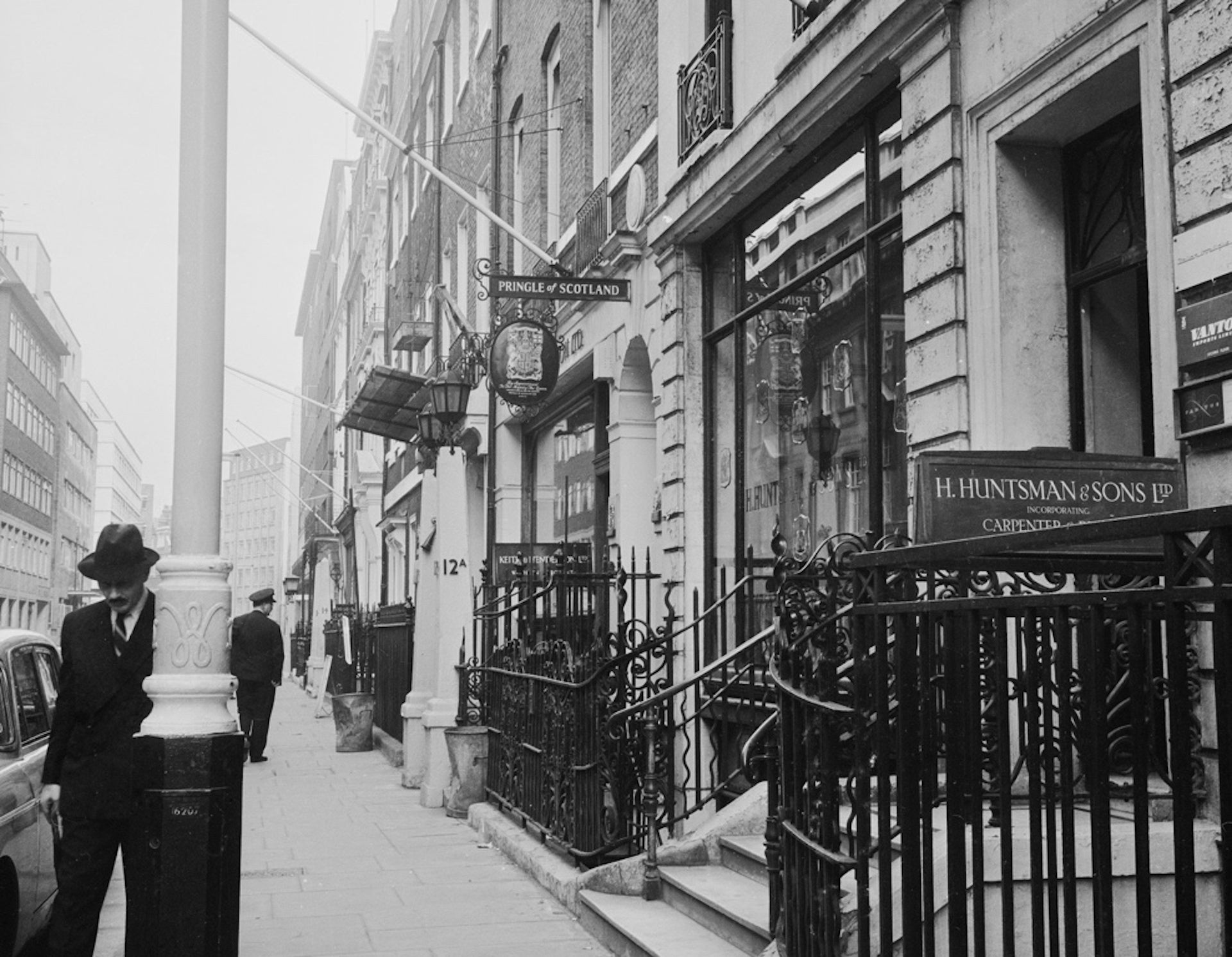 Historic photograph of Savile Row in London, with tailoring shops and pedestrians.