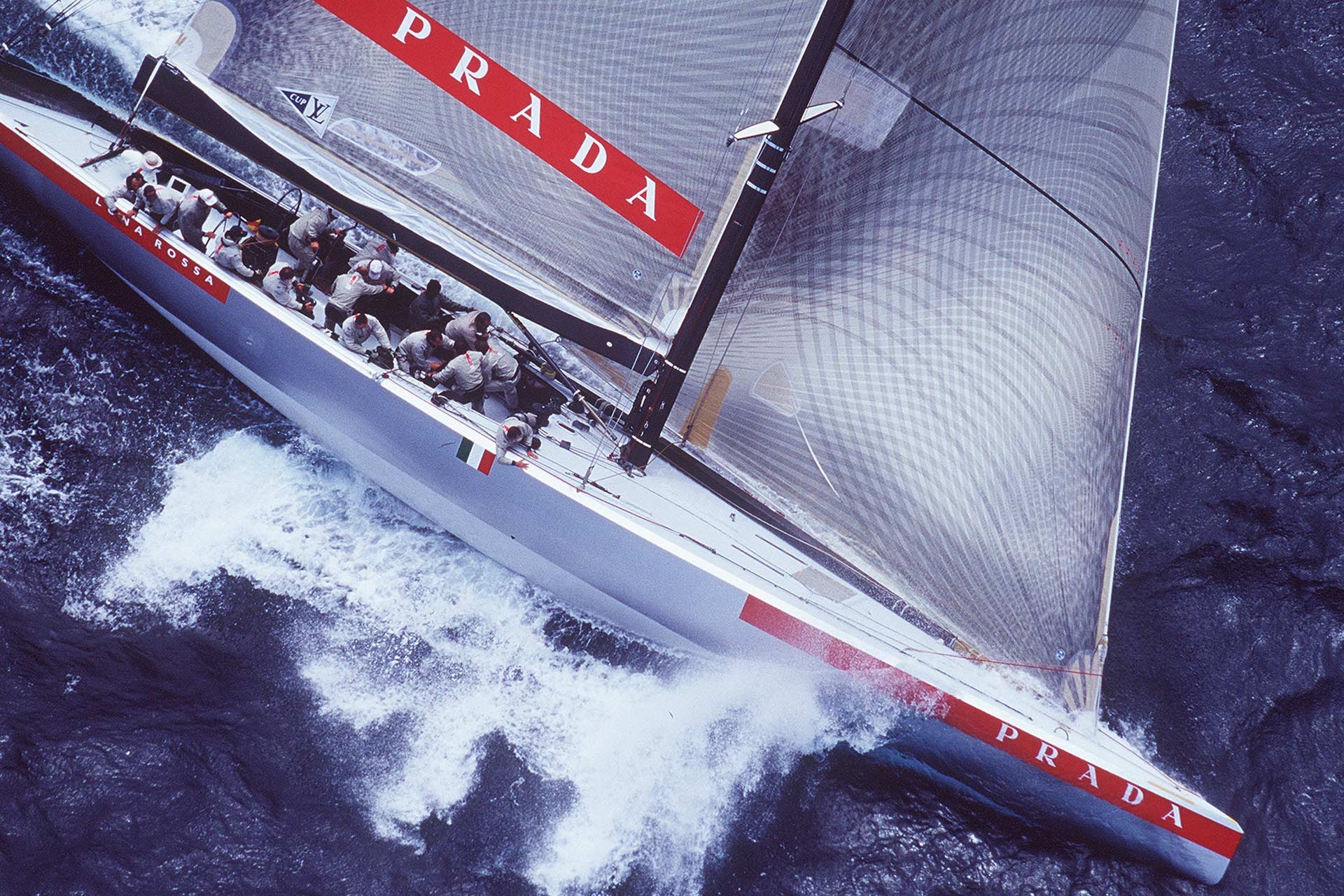 The Luna Rossa sailing yacht cuts across the sea beneath Prada-branded sails.