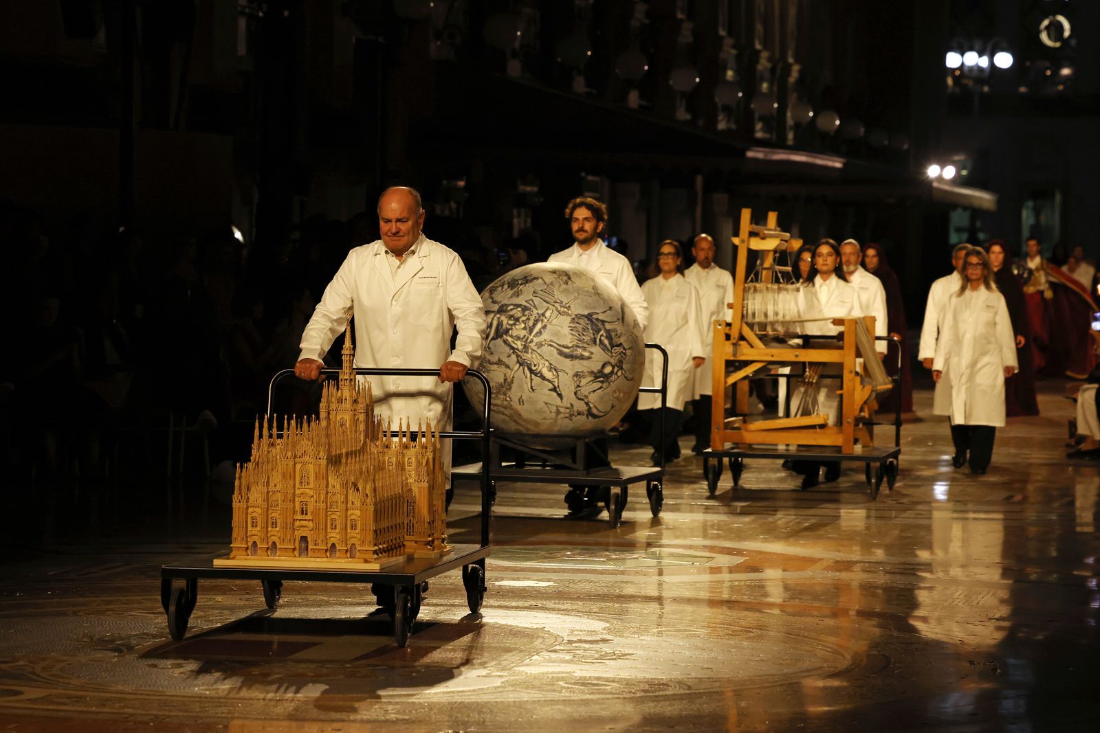 Italian artisans carrying a model of the Duomo, a celestial globe and a loom through Vogue World Milano.