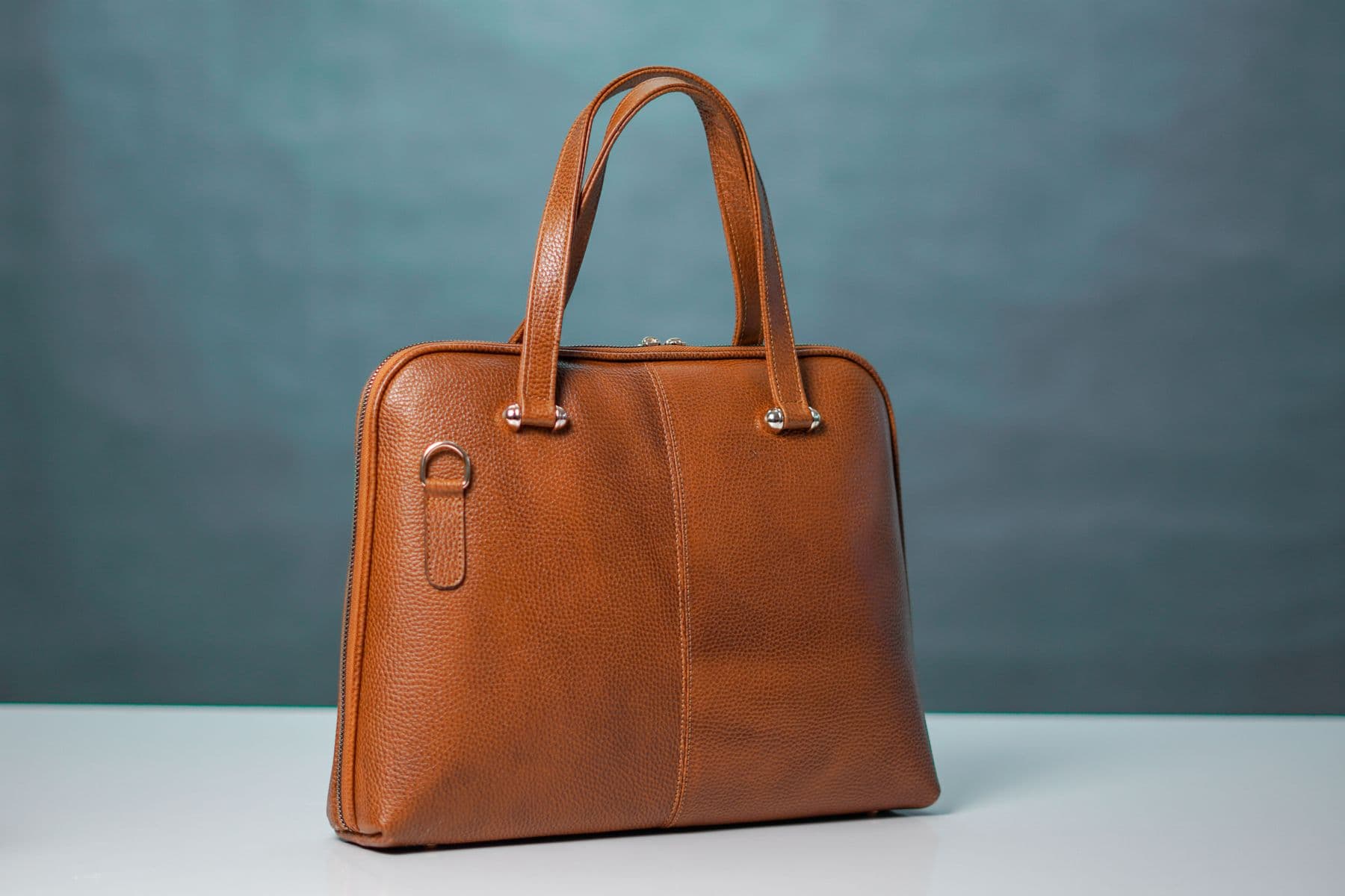 Braune Ledertasche mit sichtbaren Griffen, Nähten und Reißverschluss.