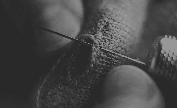 Hands guiding a needle through knitwear.