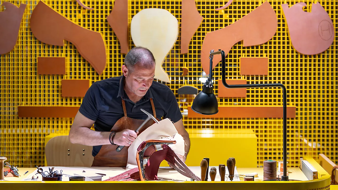 An Hermès saddler working on a leather saddle at a demonstration bench.