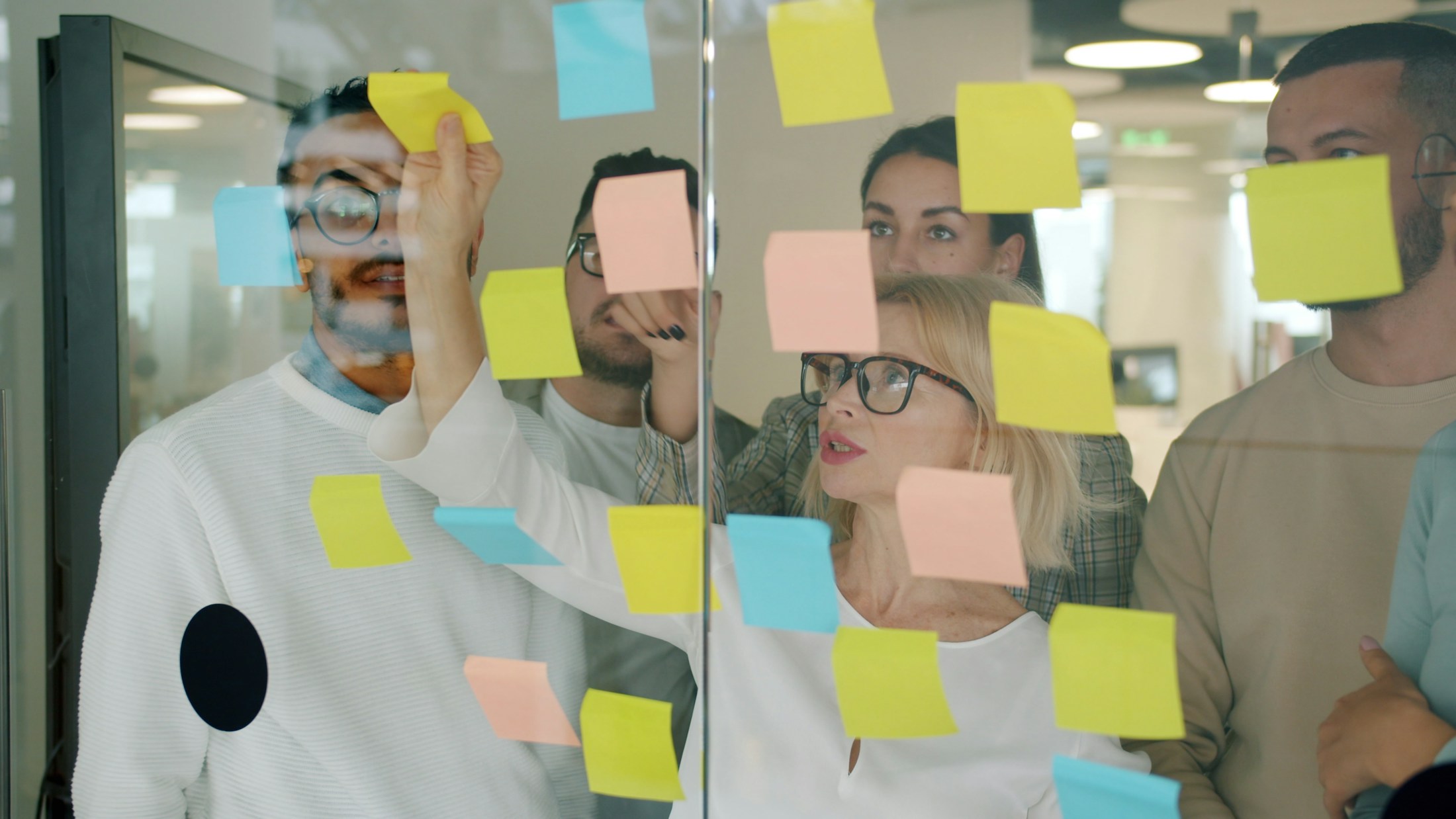 A team testing and arranging ideas with notes on a glass wall.
