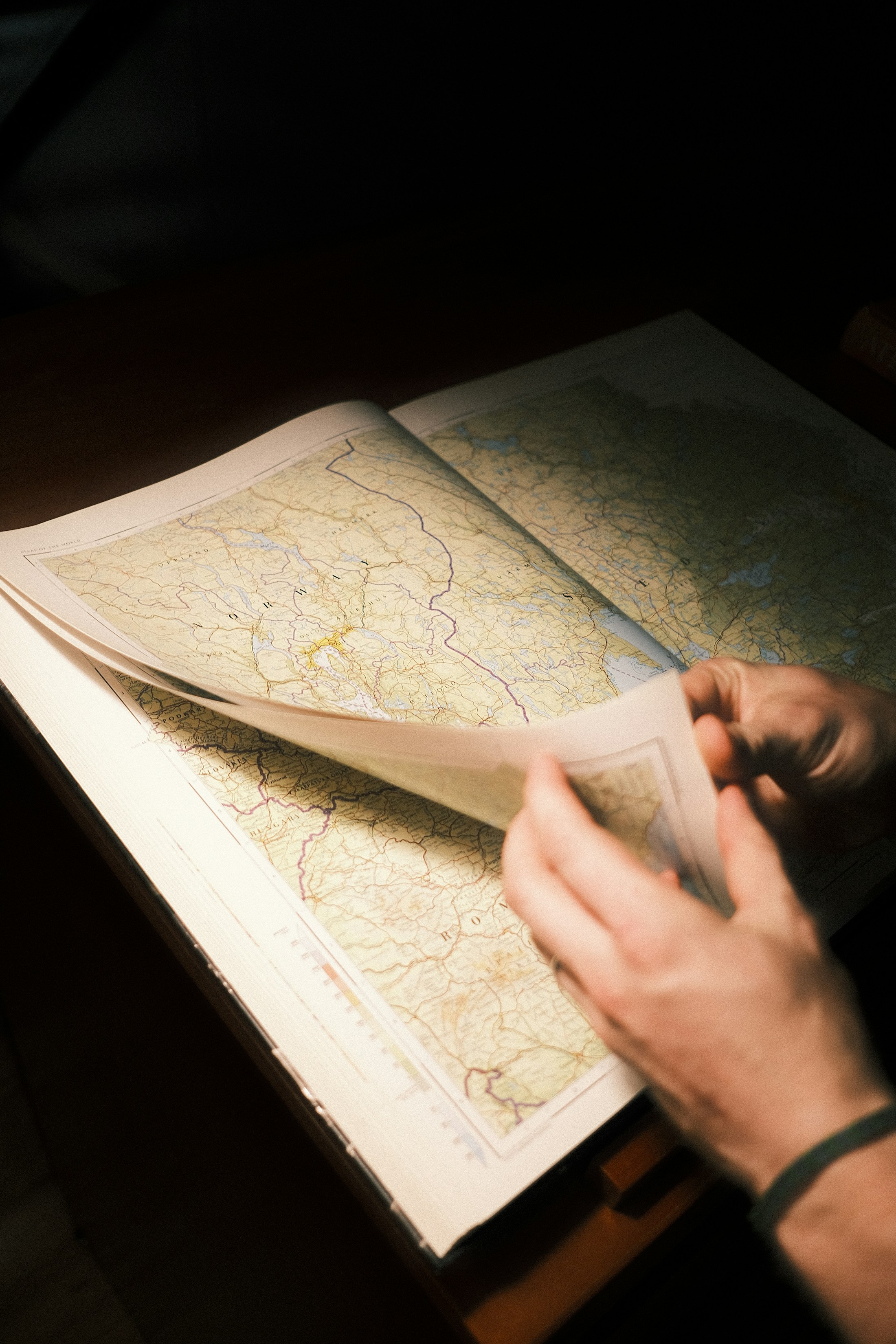 Hands turning the pages of a large atlas while exploring possible routes.