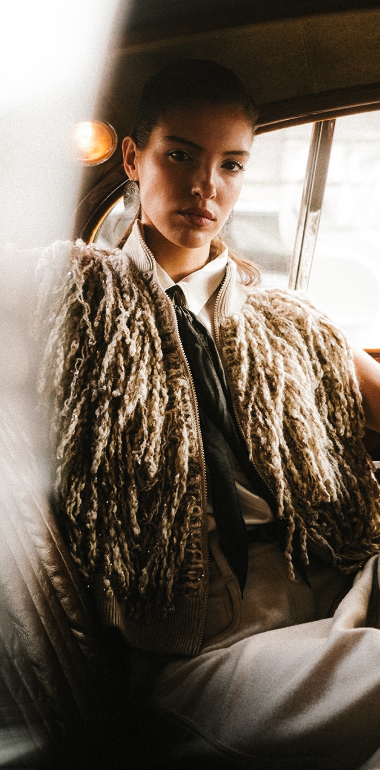 Textured cardigan over a pale shirt, seated by a vehicle window.