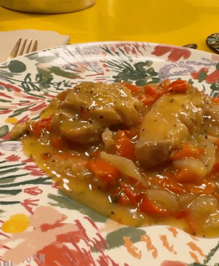 Pollo cotto con peperoni e salsa su un piatto decorato.