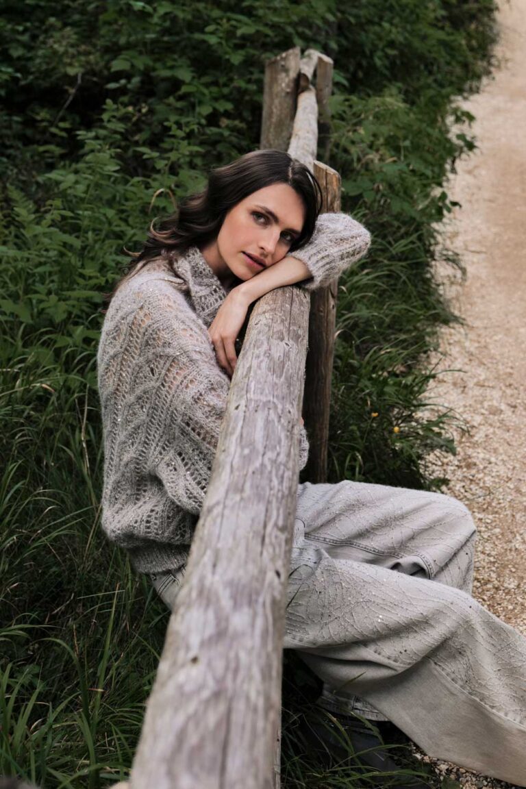 Model seated beside a wooden fence wearing textured Panicale Cashmere knitwear.